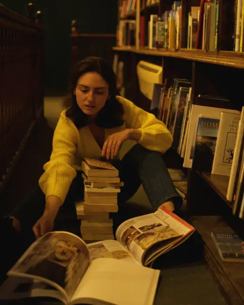 A woman sitting on the floor of a library, browsing through books