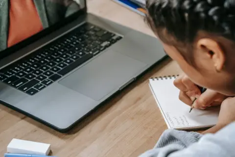 A student studying online with a laptop and writing notes